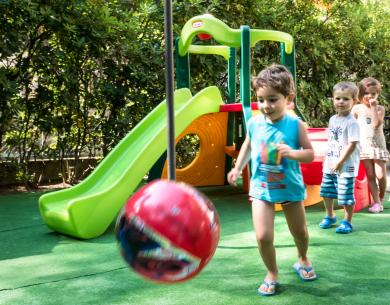 Bambini giocano felici con una palla vicino a uno scivolo colorato.