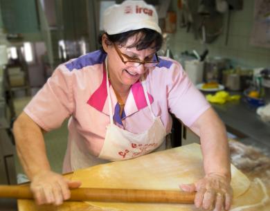 Femme étalant la pâte dans une cuisine professionnelle.
