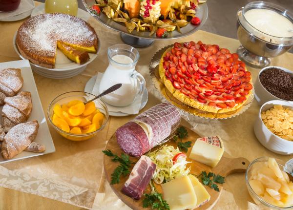 Petit-déjeuner avec pâtisseries, fruits, charcuterie, fromages et céréales.