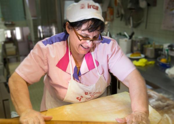 Femme étalant la pâte dans une cuisine professionnelle.